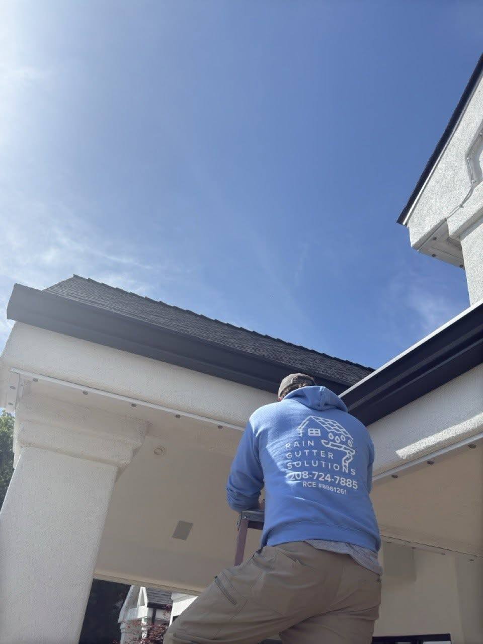 Rain Gutter Solutions crew member on a ladder fitting new gutter to a Treasure Valley home