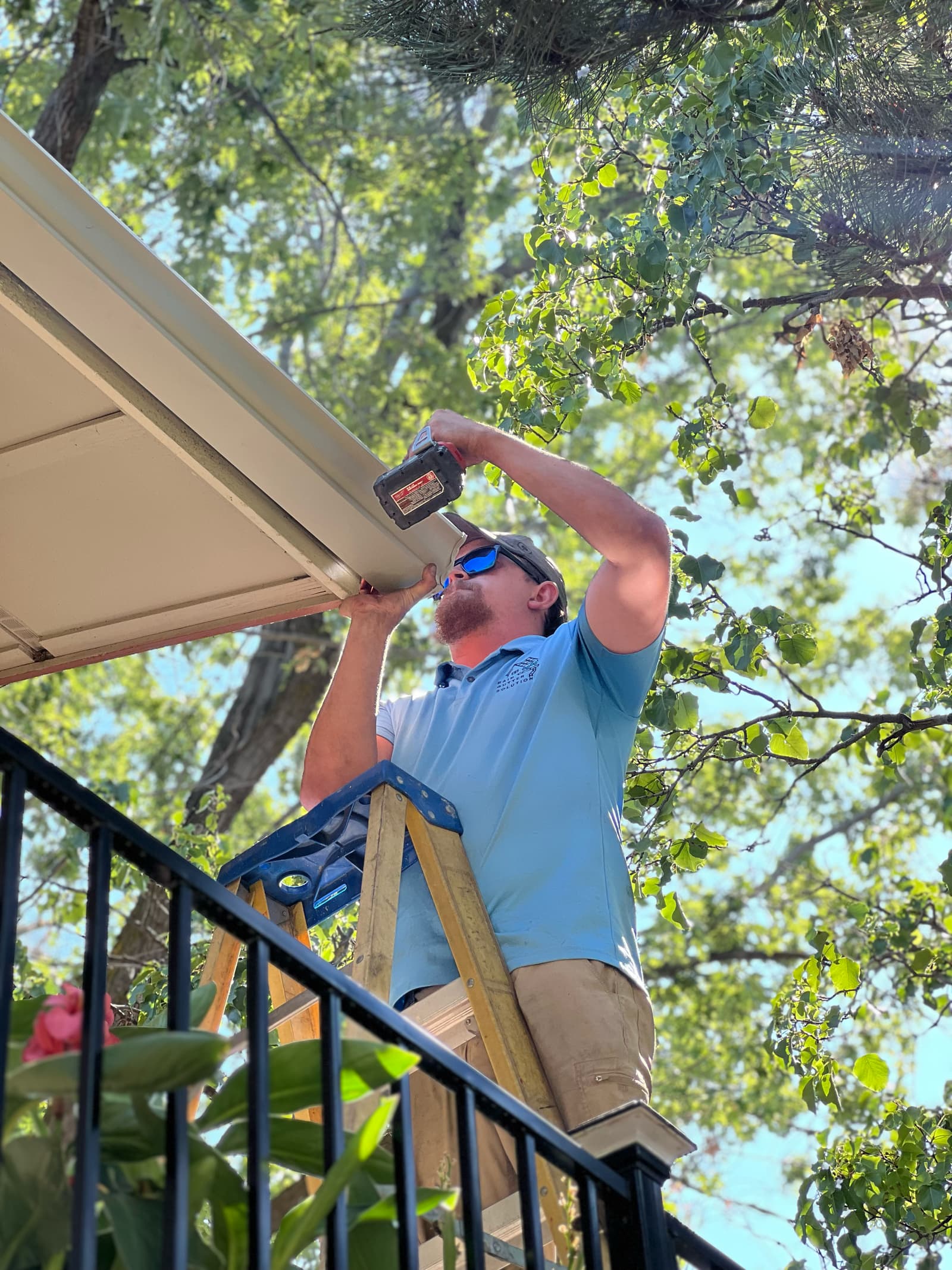 Driving a hidden hanger through the back of a new gutter run into the fascia, working off a ladder at the eave